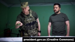 Командувач Сухопутних військ ЗСУ генерал-полковник Олександр Сирський (ліворуч) доповідає президенту України Володимиру Зеленському на позиції біля лінії фронту на Донеччині, 26 червня 2023 року