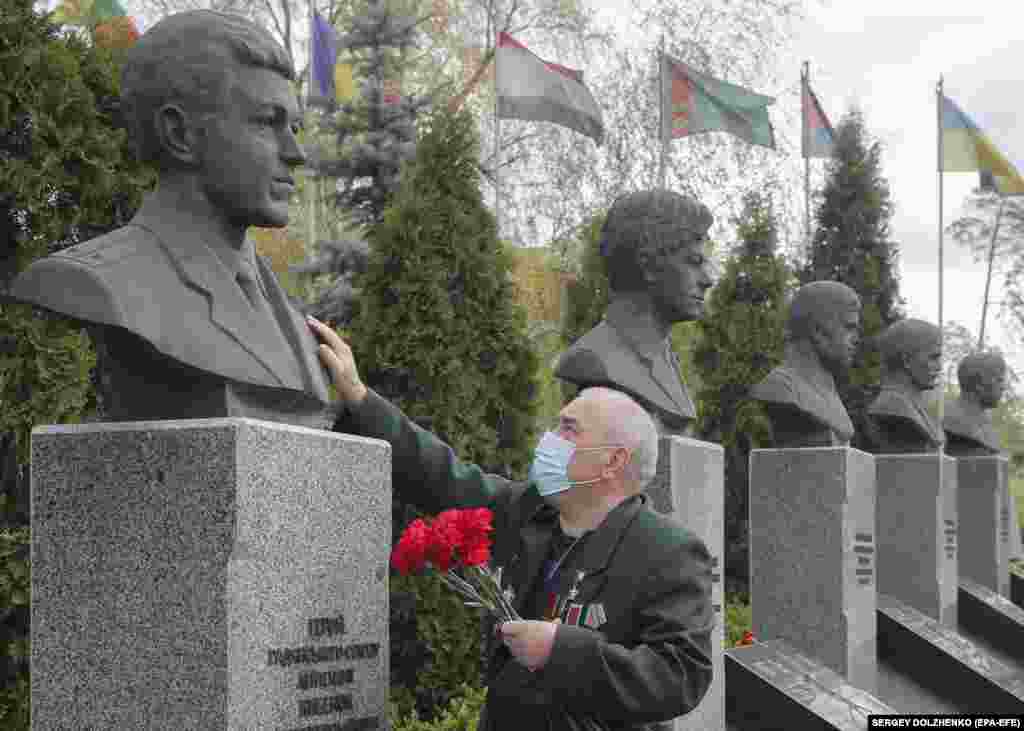 26 квітня у Києві чоловік у захисній масці і з букетом червоних квітів торкається одного з бюстів пам'ятника, присвяченого загиблим під час ліквідації наслідків аварії на Чорнобильській АЕС у 34-ту річницю трагедії. (epa-EFE/Sergey Dolzhenko)