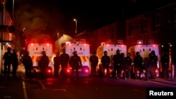 Polițiști înarmați în echipament antirevoltă stau de pază în timpul celei de-a doua nopți de revolte, în Ballymena. 10 iunie 2025.
