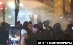 При температуре воздуха +3 градуса насквозь промокшие люди стоят под струями водометов